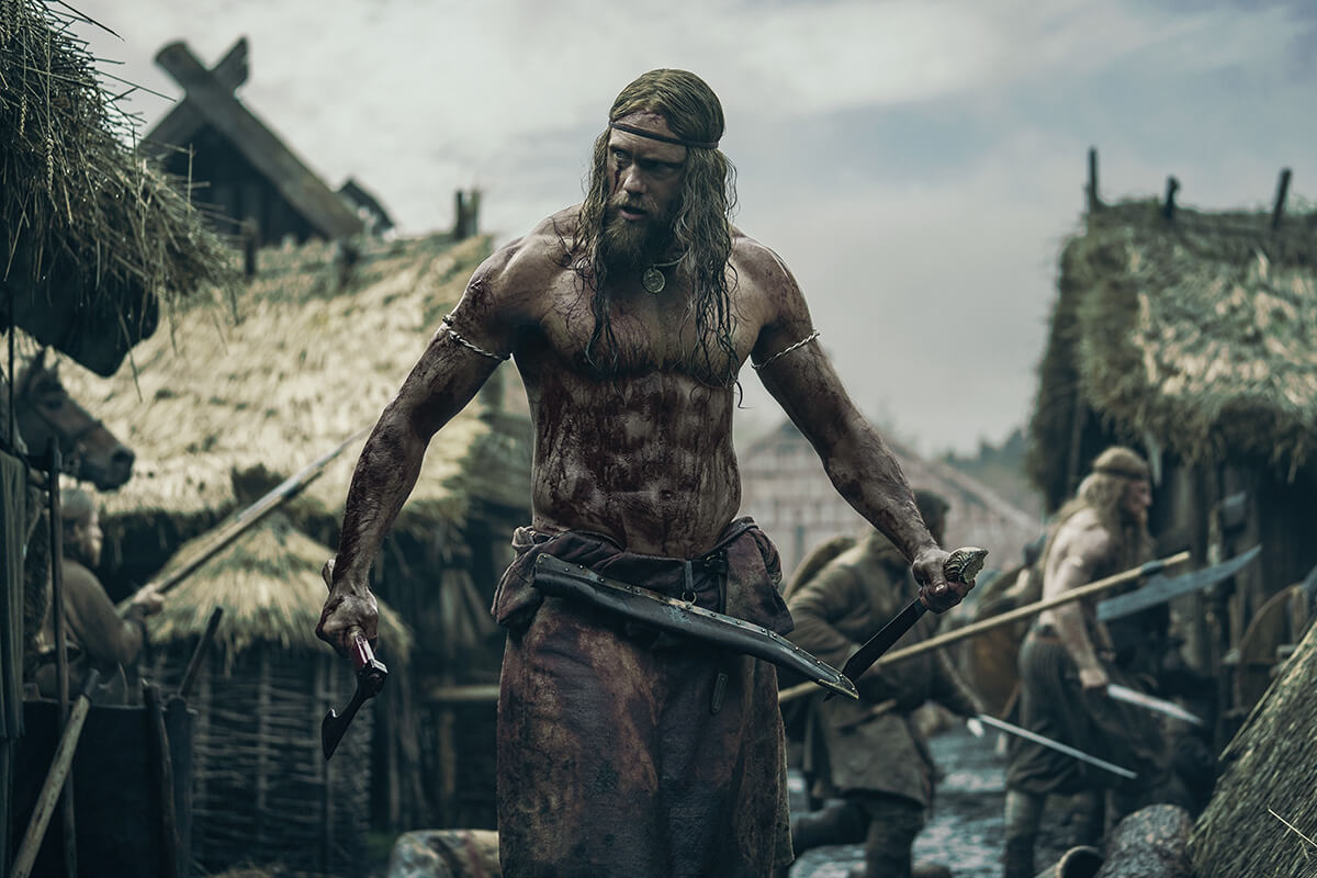 Alexander Skarsgård dressed as a viking, surrounded by hazy weather in a Danish village, playing Amleth in The Northman