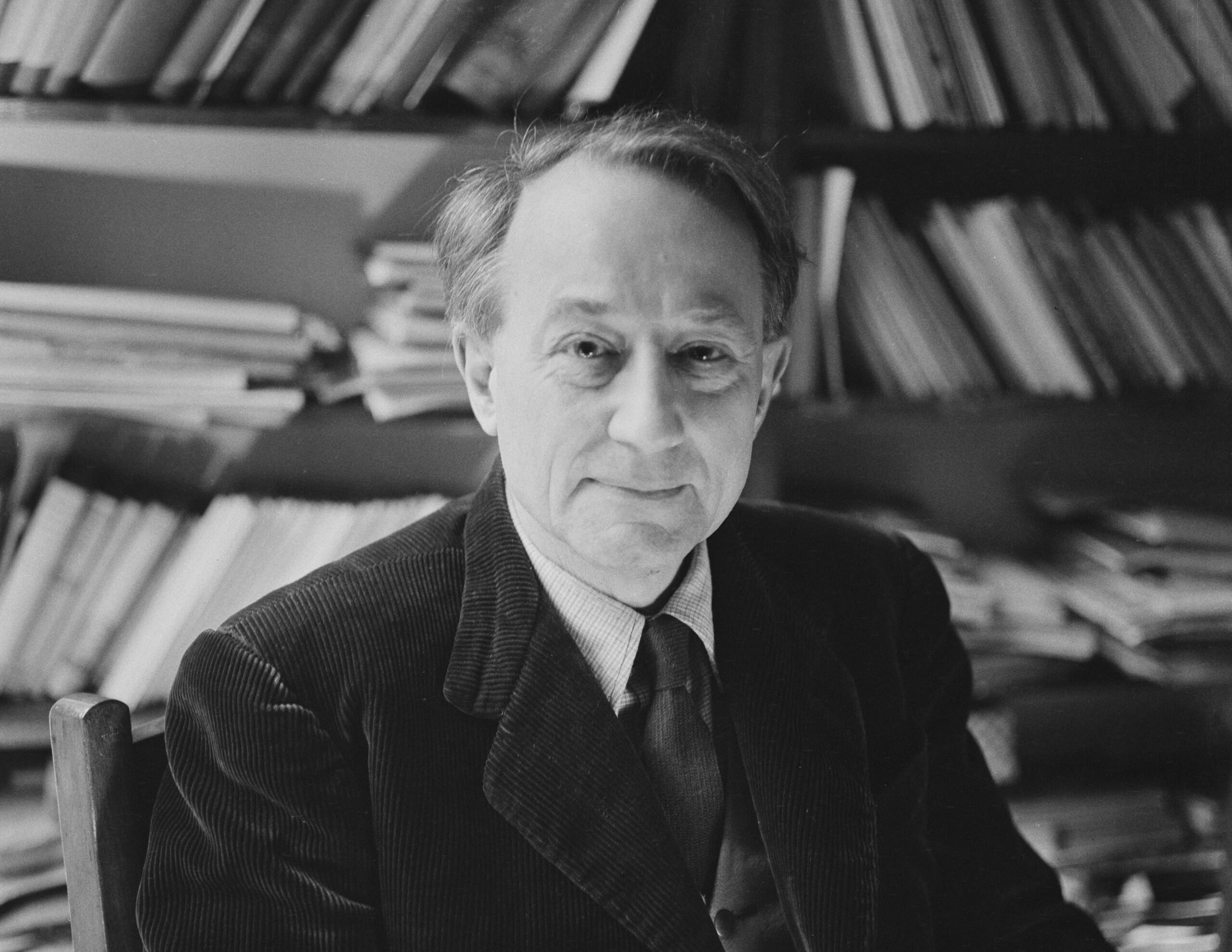 Black and white photo of a man seated in front of a bookshelf