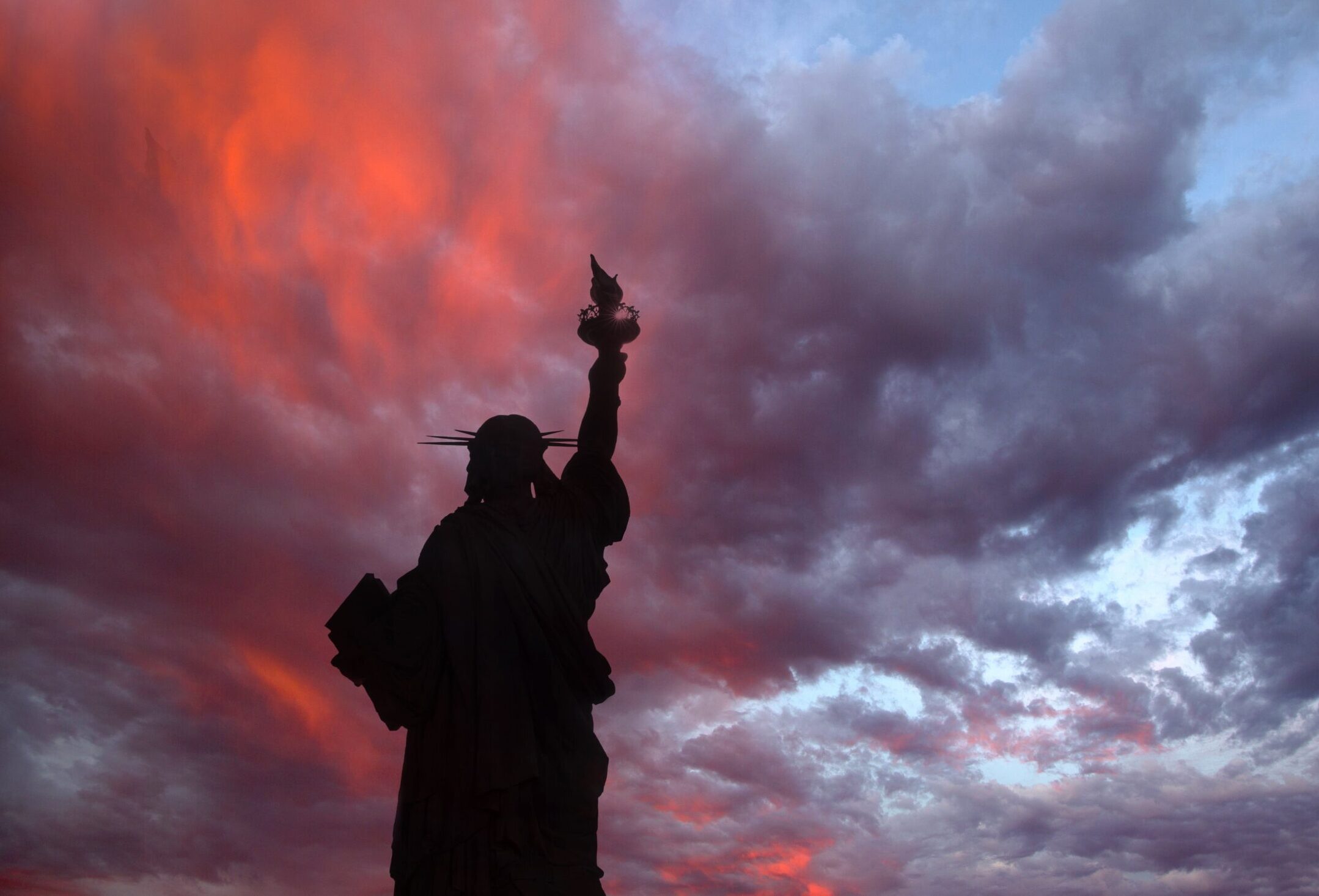 Silhouette of the statue of liberty against a cloudy sky